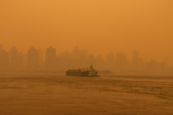 A barge on a New York City river and skyscrapers, all blurred by orange-gray smoke from massive wildfires